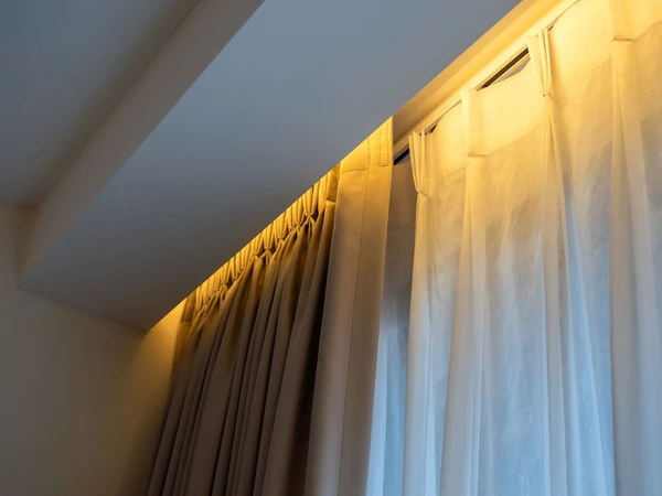 Close-up view of dual-layer winter curtains featuring beige blackout fabric and sheer white voile under warm ceiling light in a Dubai interior.