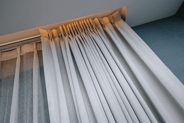 Close-up of premium track-mounted curtains with sheer gauze layer and structured pinch pleats in a modern Dubai home.

