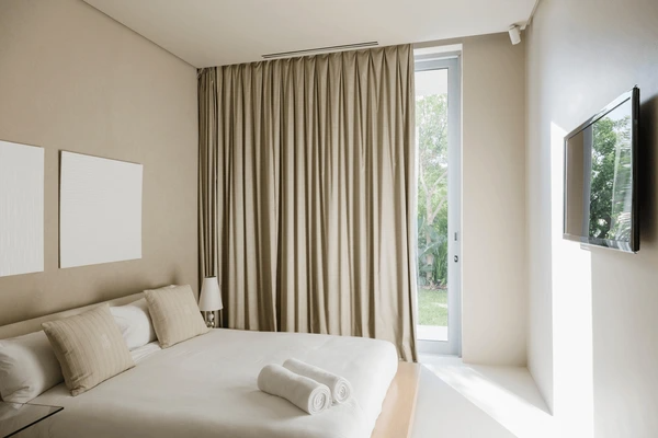 Modern Dubai bedroom with beige blackout curtains, white linens, and soft natural lighting for a serene and elegant resort-style feel.