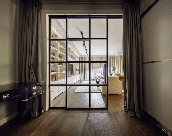 Sophisticated Dubai interior with floor-length curtains framing sliding glass doors, blending traditional luxury with modern shelving and spacious layout.

