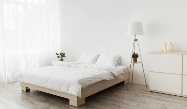Minimalist Dubai bedroom with white walls, sheer curtains, wooden bed frame, and modern floor lamp.