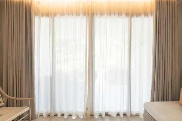 Elegant soft beige blackout curtains paired with white sheer panels, framing a sunlit window in a cozy modern Dubai home.

