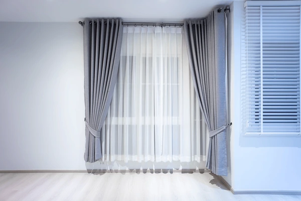 Elegant grey blackout curtains layered with sheer white drapes against pristine white walls in a modern Dubai home.


