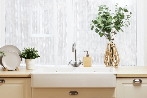 A cozy kitchen with a farmhouse-style sink and sheer lace café curtains letting in soft natural light.