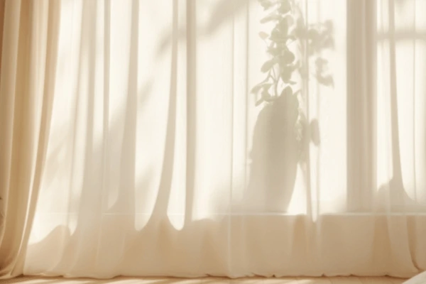 Soft beige sheer curtains in a sunlit Dubai room with a potted plant’s shadow falling gently across the fabric.

