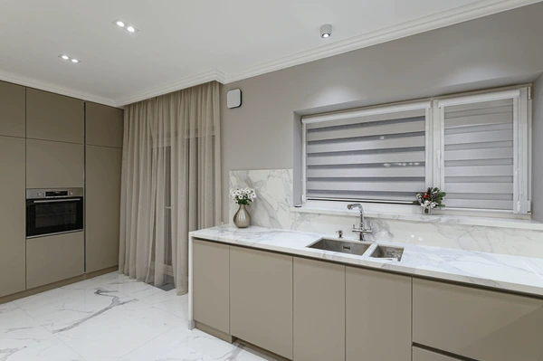 Luxurious modern kitchen in Dubai with marble countertops, sheer falling curtains, and layered zebra blinds.