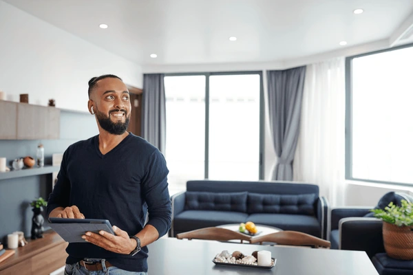 Contemporary living room in Dubai with elegant long curtains, navy sofa, large windows, and a smiling man holding a tablet.