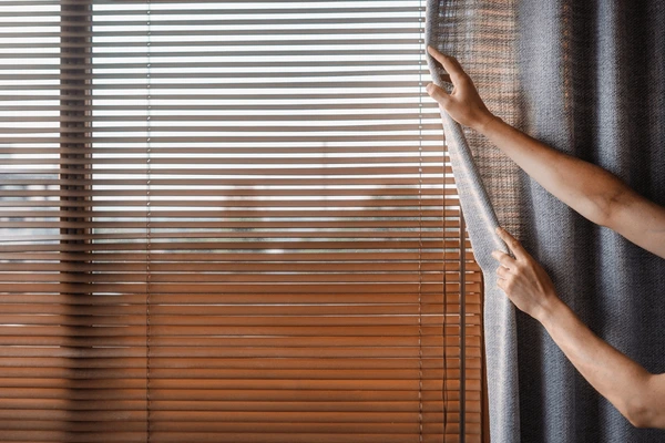 Person adjusting modern grey curtain beside stylish horizontal blinds, showcasing the best affordable curtains and blinds in Dubai 2025 for elegant and cozy interiors.
