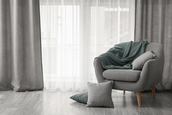 Modern living space with grey wall curtains, armchair, and soft furnishings in Dubai 2025.
