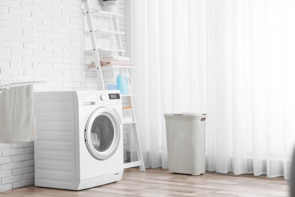 A bright laundry room with a modern washing machine and sheer white curtains, showcasing stylish and easy-to-clean home textiles in Dubai.