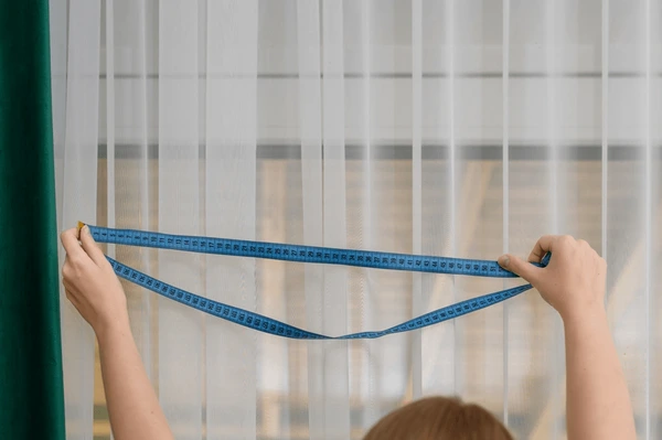 Professional measuring elegant beige curtains for custom fitting in a sleek modern Dubai home interior 2025.