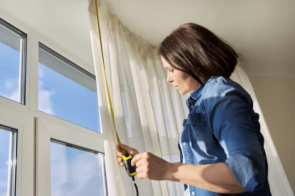 Woman measuring curtain height with tape in bright modern home for custom-fit luxurious curtains in Dubai 2025.
