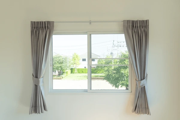 Light grey velvet curtains tied back on a small window in a modern Dubai home, 2025.