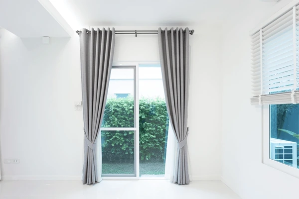 Soft grey blackout curtains in a bright white modern room with a large glass door, styled for a cozy Christmas look in Dubai 2025. Best blackout curtains for privacy, insulation, and home comfort.