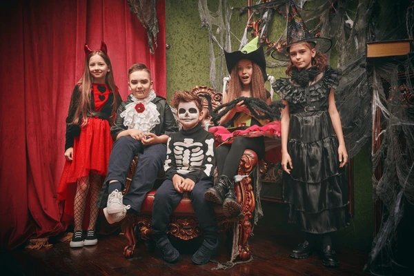 Children in Halloween costumes posing in front of red curtains and cobweb decorations during a festive celebration in Dubai 2025.