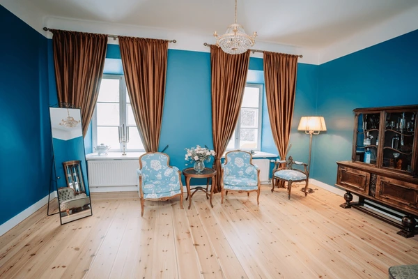 Traditional Dubai living room with gold velvet curtains, blue walls, antique wooden furniture, and vintage armchairs.