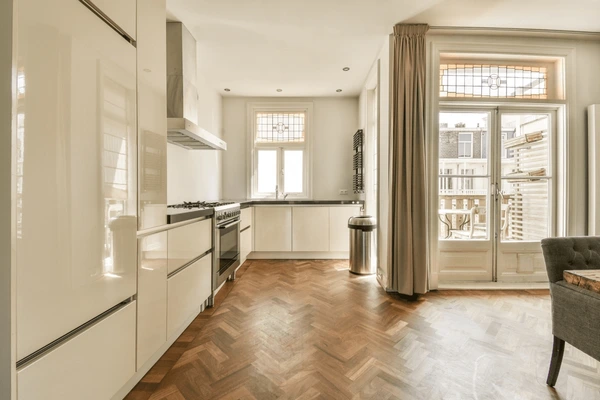 Modern kitchen in Dubai with traditional beige curtains, wooden flooring, and sleek white cabinets offering a cozy yet stylish aesthetic.